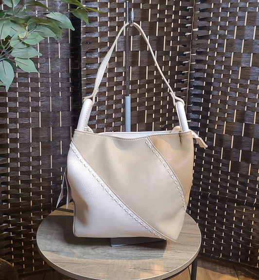 Bolso de polipiel beige claro con costuras en diagonal sobre mesa de madera, fondo de panel decorativo.